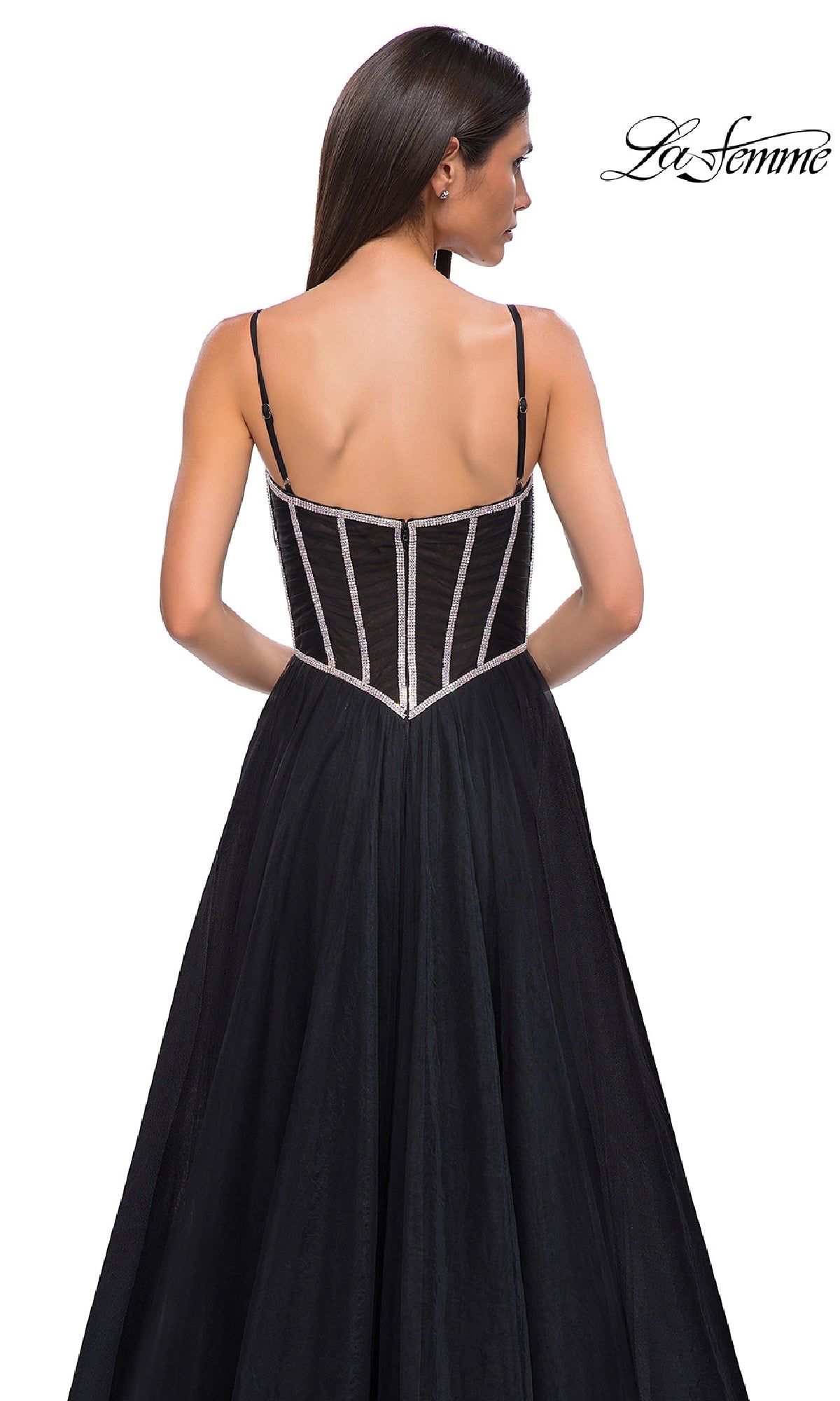 A woman faces away in the Long Corset Prom Ball Gown: La Femme 32675, a black strapless gown with visible boning and thin straps, set against a white background. The 
