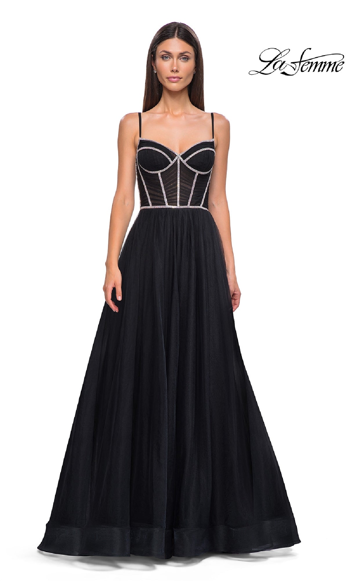 Woman in a black Long Corset Prom Ball Gown: La Femme 32675 with a sheer corset-style bodice and thin straps, standing against a white backdrop. 