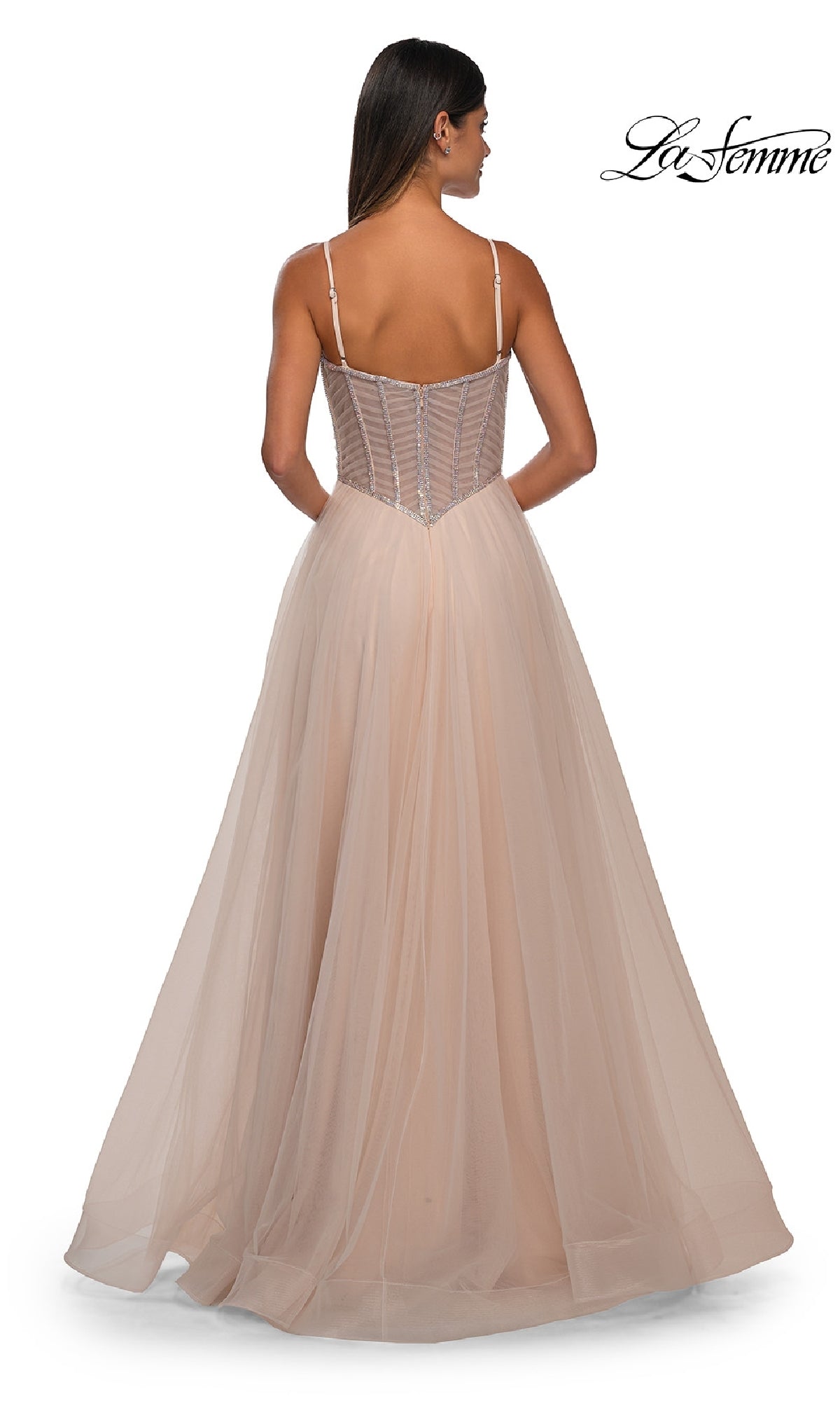 A woman is shown from the back wearing the Long Corset Prom Ball Gown: La Femme 32675—a floor-length blush a-line dress with a sheer corset bodice, spaghetti straps, and a full tulle skirt for an elegant look.