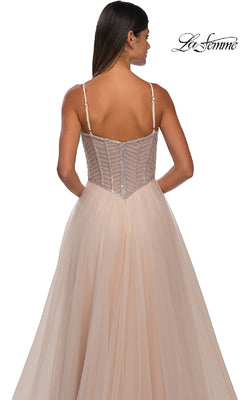 A woman in a blush pink Long Corset Prom Ball Gown, La Femme 32675, featuring a fitted sheer corset back and thin straps, stands against a white background.
