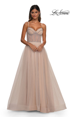 A woman wears the Long Corset Prom Ball Gown: La Femme 32675, a light beige, floor-length A-line dress with thin straps and a structured bodice, standing against a plain white background. "La Femme" logo appears in the top right corner.