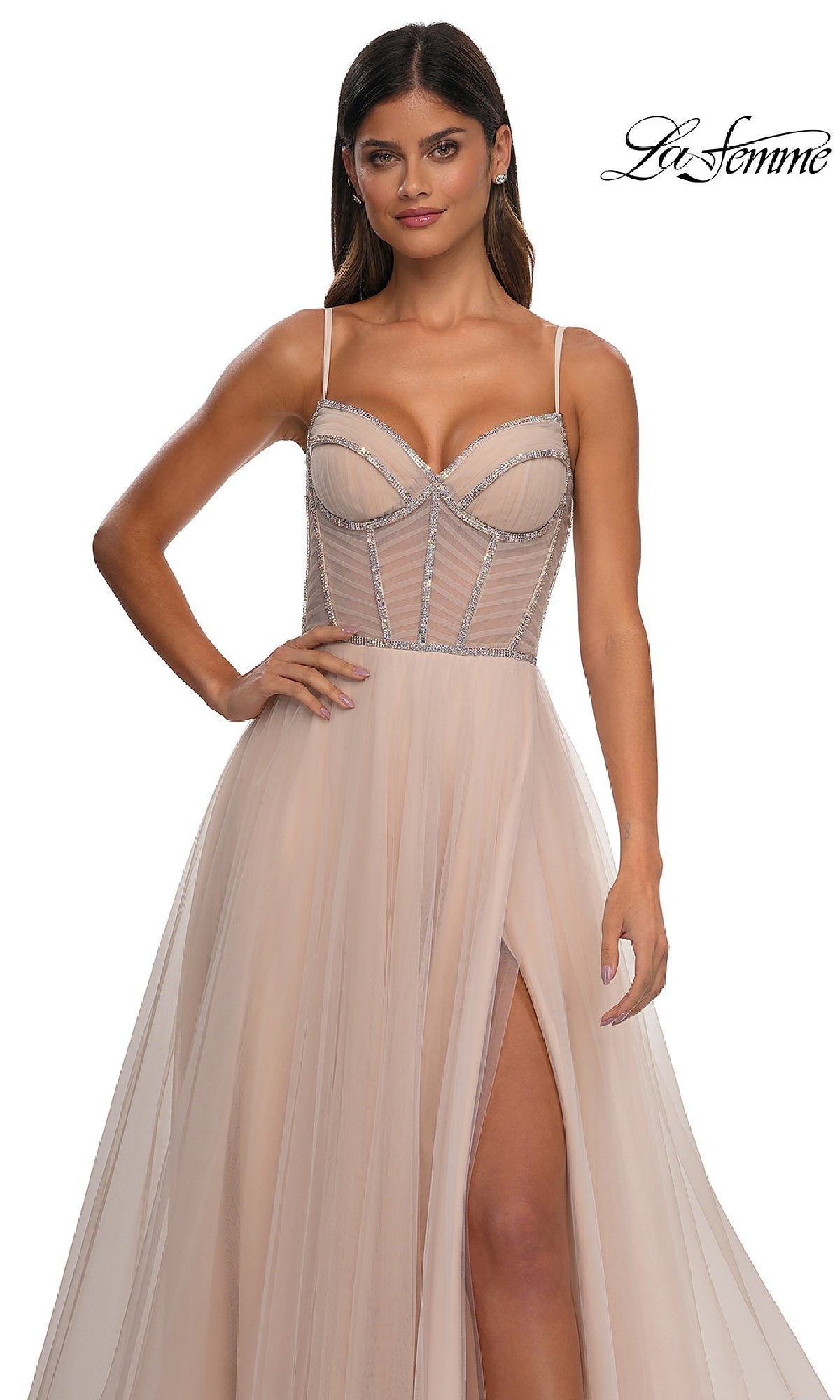A woman wears the Long Corset Prom Ball Gown: La Femme 32675, a light beige A-line dress with thin straps, rhinestone-trimmed bodice, and high thigh slit; 