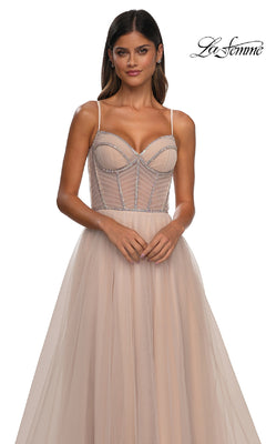 A woman wears the Long Corset Prom Ball Gown: La Femme 32675 in light beige, featuring a sleeveless a-line design with sheer bodice and thin straps, standing against a white background. "La Femme" logo appears in the top right corner.