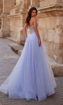 A woman poses outdoors by a stone building in the Long Corset Prom Ball Gown: La Femme 32675, featuring a fitted bodice and flowing tulle skirt.