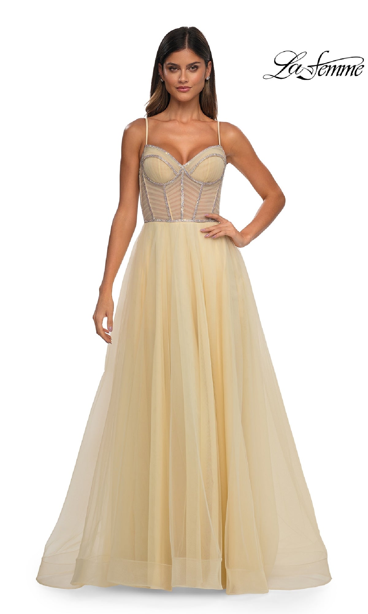 A woman wears the La Femme 32675, a long yellow sheer tulle prom ball gown with thin straps and a structured corset bodice. The elegant A-line dress radiates timeless glamour. “La Femme” logo appears in the top right corner.