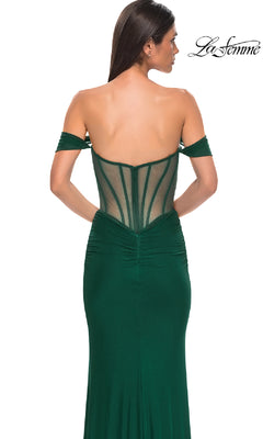 A woman models the La Femme 32684 Off-the-Shoulder Corset Prom Gown in emerald green, featuring a fitted design and sheer corset back, elegantly displayed from behind.