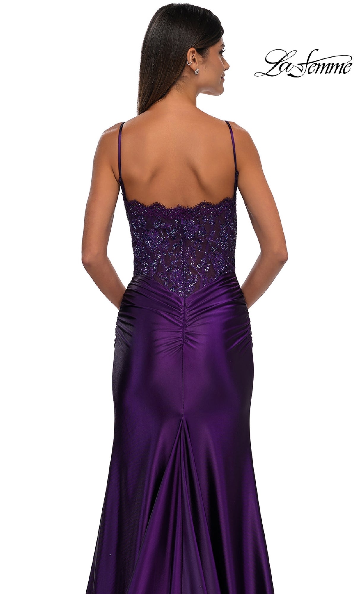 Woman wearing the Glitter-Bodice Long Prom Dress La Femme 32689, a fitted deep purple gown with thin straps, a glitter bodice, and lace detailing on the upper back, standing with her back to the camera.
