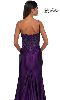 Woman wearing the Glitter-Bodice Long Prom Dress La Femme 32689, a fitted deep purple gown with thin straps, a glitter bodice, and lace detailing on the upper back, standing with her back to the camera.