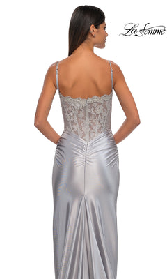 Woman in a form-fitting La Femme 32689 Glitter-Bodice Long Prom Dress, silver with lace-detailed back, thin straps, and ruched fabric below the waist—she faces away from the camera.