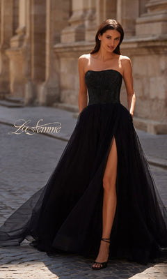 A woman wears the "Strapless Long Prom Ball Gown" La Femme 32690 on a cobblestone street in front of a stone building. The text "La Femme" is displayed on the left side.