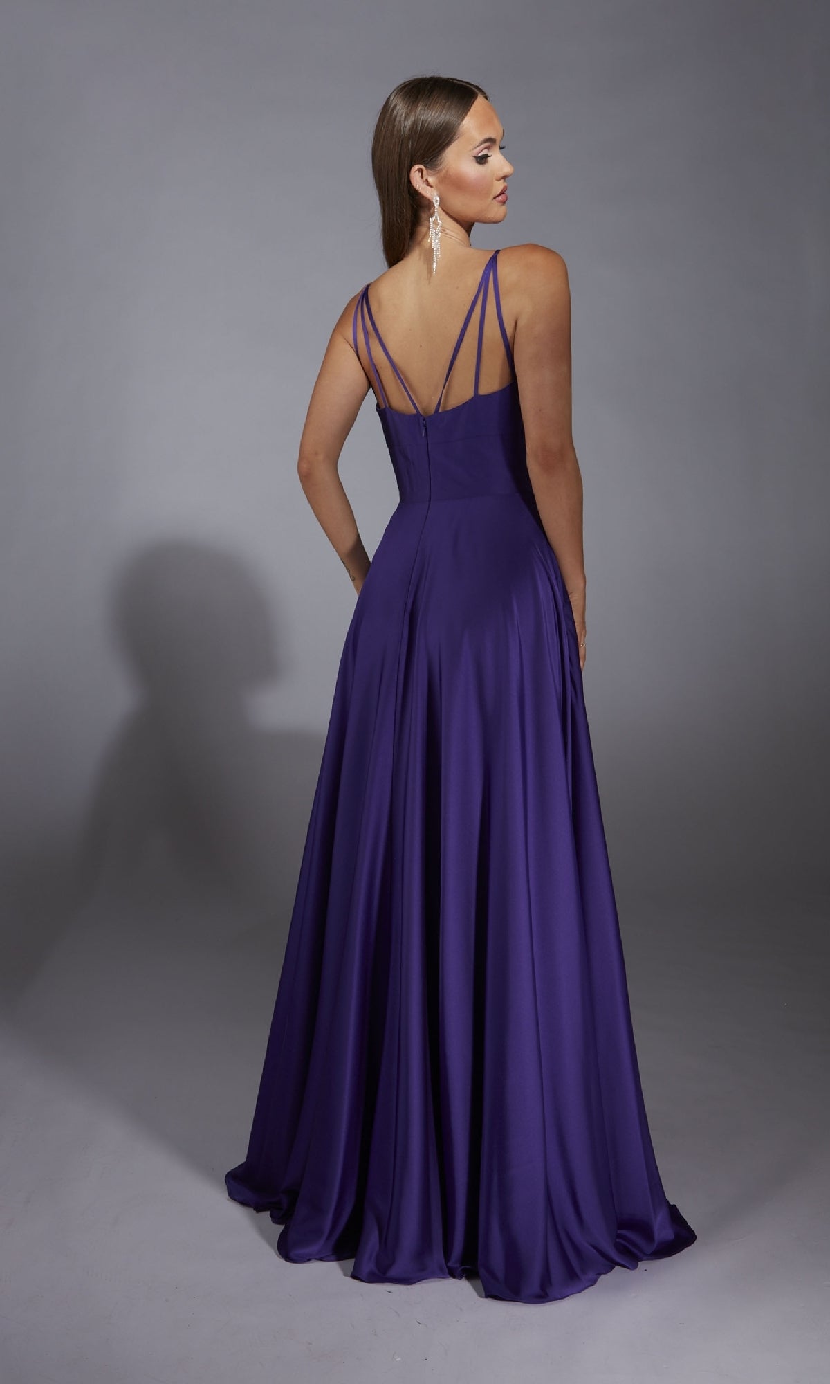A woman in the Aerie Couture 326 long formal dress stands facing away, displaying its sleeveless, floor-length a-line silhouette, thin straps, open back, and flowing skirt against a plain gray background.