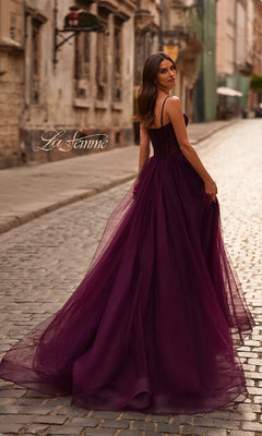 A woman walks on a cobblestone street lined with old buildings, wearing the La Femme 32700 Tulle Prom Ball Gown with Pockets in dark purple.