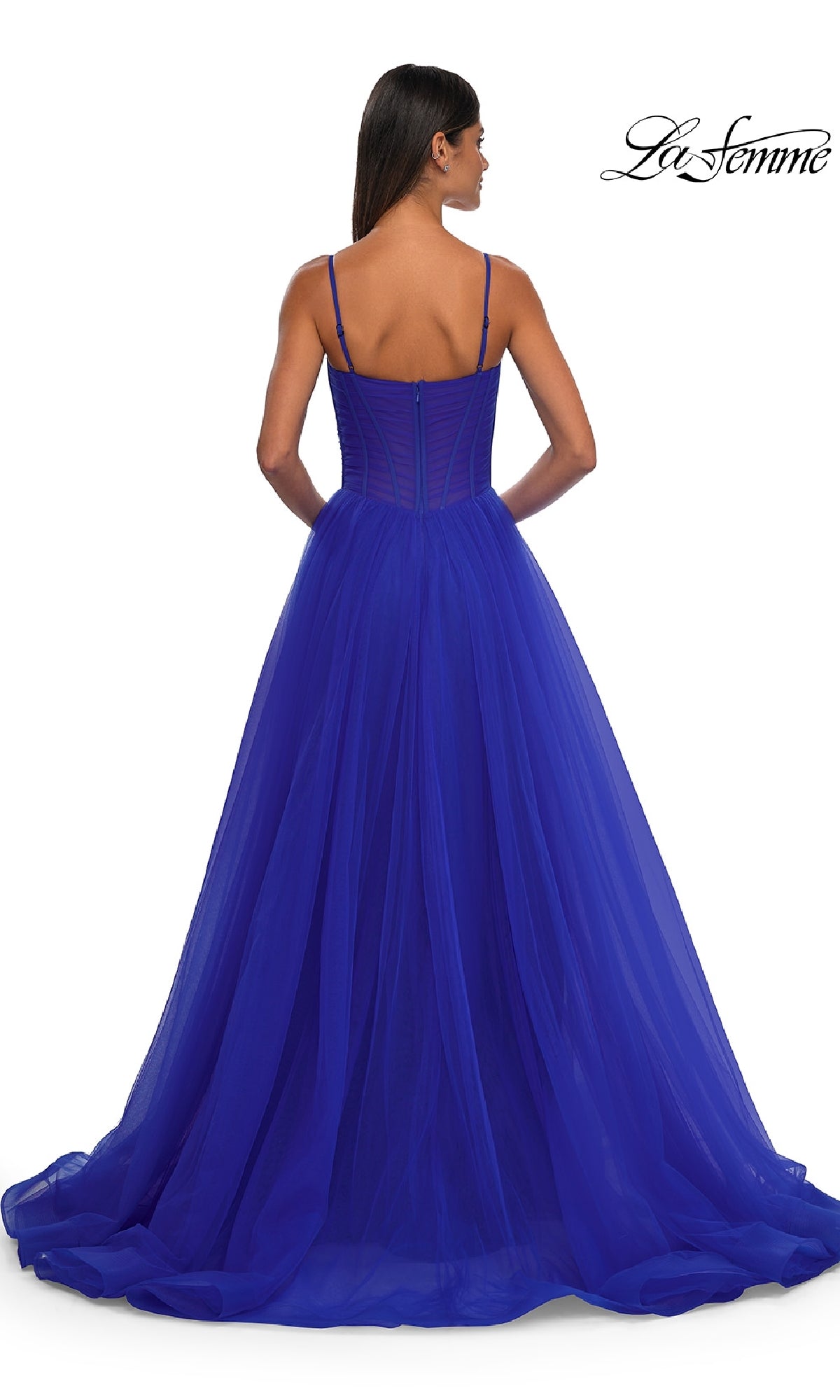 A woman in the La Femme 32700 Tulle Prom Ball Gown with Pockets, royal blue and floor-length with thin straps, stands facing away to show its flowing a-line skirt and fitted bodice.