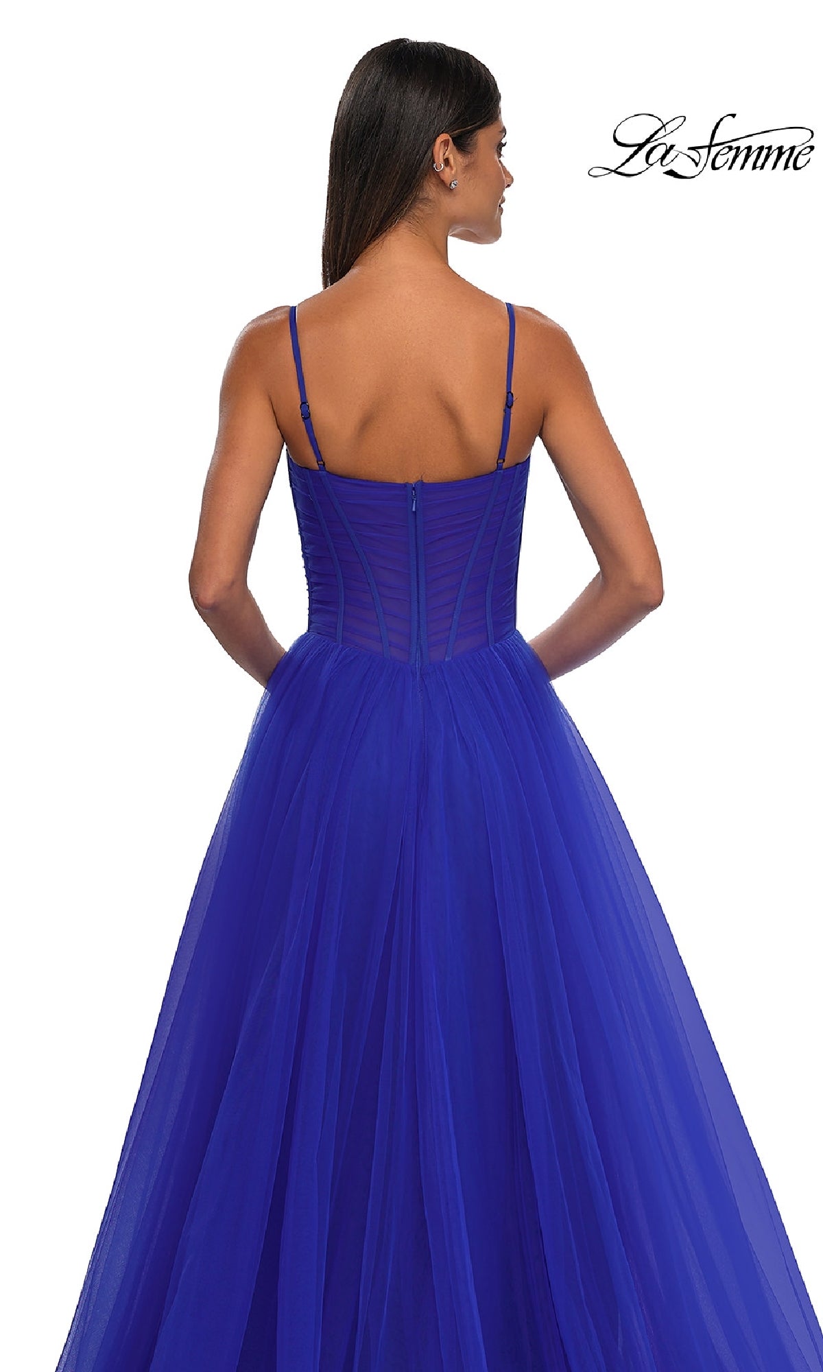 A woman faces away, wearing the La Femme 32700 Tulle Prom Ball Gown with Pockets in royal blue. This floor-length A-line dress features thin straps, a sheer corset-style bodice, and a white backdrop with the 