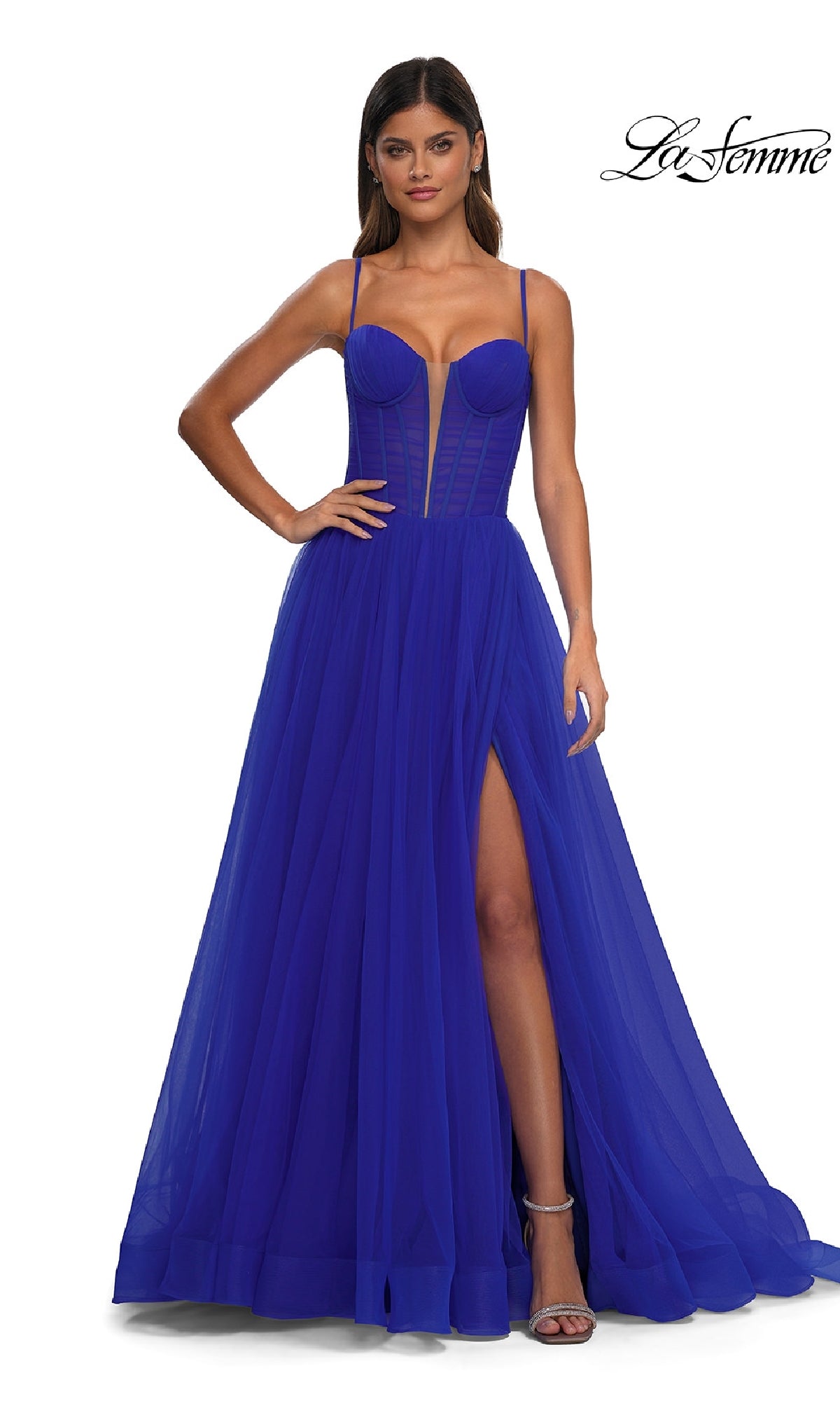 A woman wears the La Femme 32700 Tulle Prom Ball Gown with pockets, a royal blue floor-length dress with spaghetti straps, structured sheer corset bodice, and high slit; “La Femme” logo appears in the top right corner.