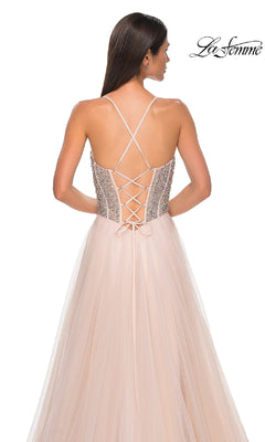 A woman models the La Femme 32703 Beaded-Corset Long Prom Dress, a sleeveless blush A-line gown with rhinestone-beaded corset back, crisscross straps, and tulle skirt. The La Femme logo is shown in the top right corner.