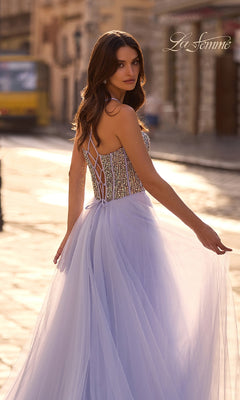 A woman wearing the La Femme 32703 Beaded-Corset Long Prom Dress, a sleeveless lavender A-line gown with a lace-up back and rhinestone corset, stands on a sunlit city street looking over her shoulder.