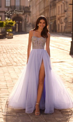 A woman in the Beaded-Corset Long Prom Dress: La Femme 32703 with a rhinestone-bedecked corset and thigh-high slit smiles at the camera while standing on a cobblestone street.
