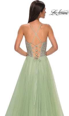 A woman wears the Beaded-Corset Long Prom Dress: La Femme 32703—a sage green, floor-length A-line gown with a lace-up open back, crisscross straps, and rhinestone-beaded bodice—posing against a white background.