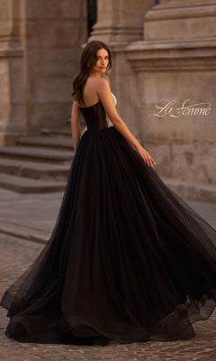 A woman in the La Femme 32704 long prom dress with a strapless bodice and flowing tulle skirt stands on a cobblestone street, glancing over her shoulder.