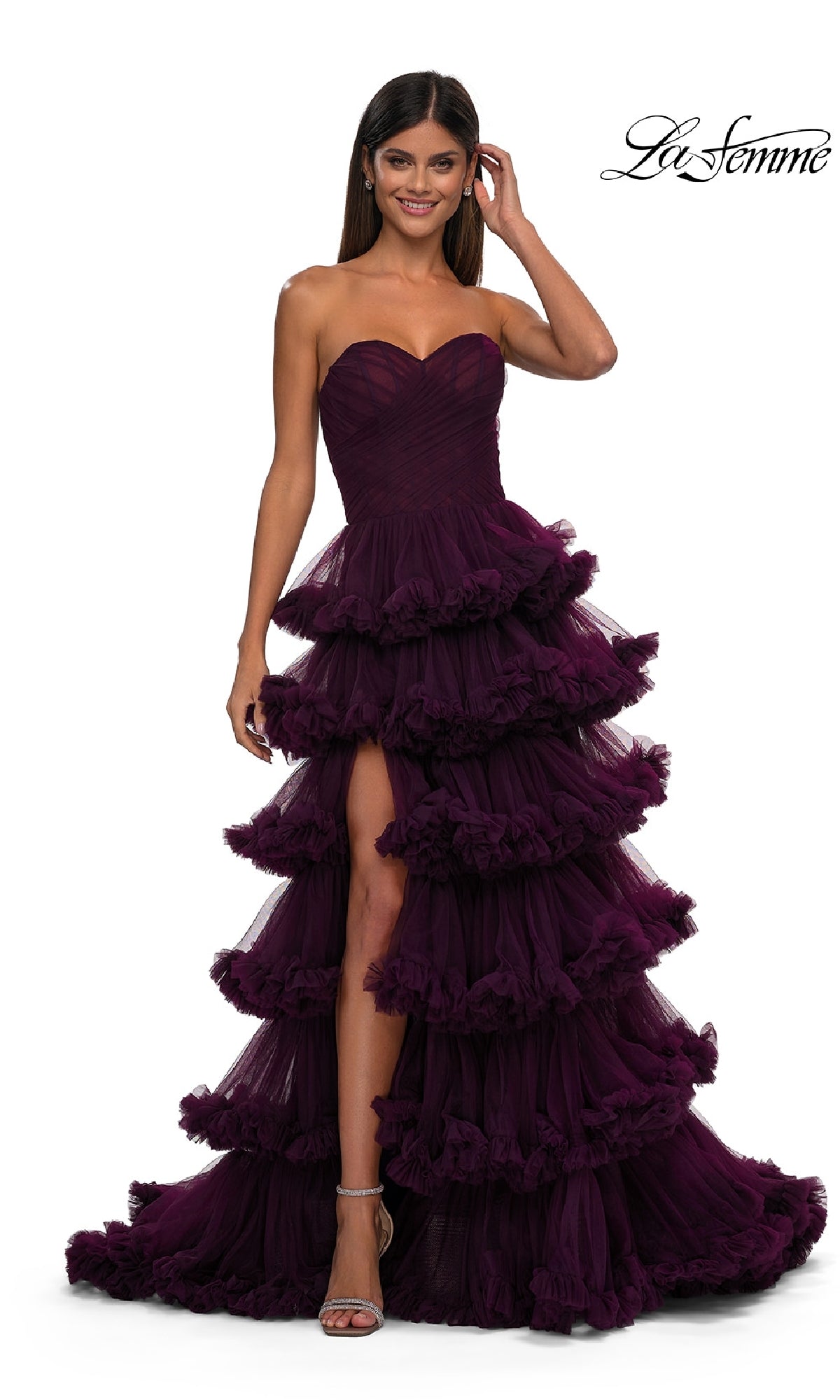 A woman in the Strapless Ruffled Prom Ball Gown: La Femme 32721, a dark purple long dress with ruffles and a high slit, smiles against a white background. The La Femme prom dress logo is in the top right corner.