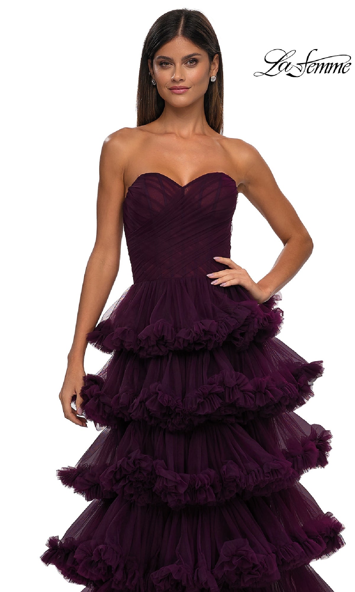 A woman poses against a white background in the Strapless Ruffled Prom Ball Gown: La Femme 32721, featuring dark purple tulle with multiple ruffled tiers. The 