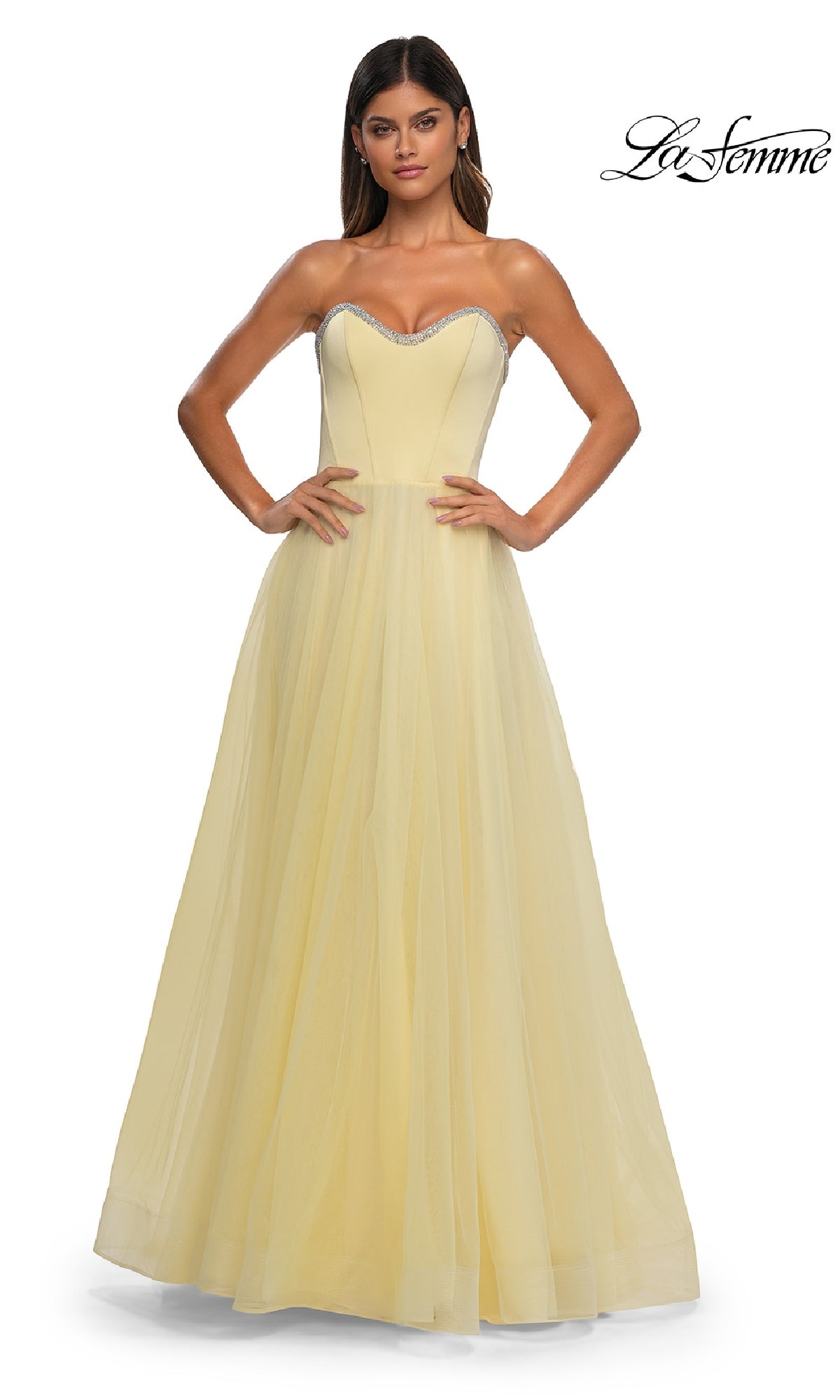 A woman wears the Strapless Long Prom Ball Gown: La Femme 32731, a light yellow, floor-length dress with a sweetheart neckline, fitted bodice, and full tulle skirt; 