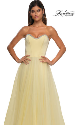A woman wears the La Femme 32731 Strapless Long Prom Ball Gown in light yellow, featuring a fitted bodice, tulle skirt, silver-trimmed sweetheart neckline, and the "La Femme" logo in the top right corner.