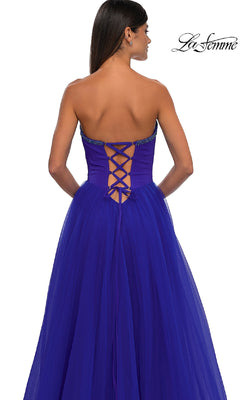 A woman models the La Femme 32731 strapless long prom ball gown in royal blue, shown from behind to highlight the sweetheart neckline, floor-length skirt, and elegant lace-up back detail.