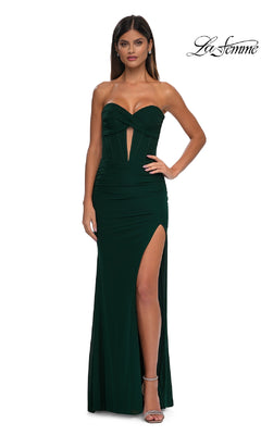 A woman wears the Cut-Out Long Strapless Prom Dress: La Femme 32734 in dark green, featuring a sweetheart neckline, front cutout, thigh-high slit, and paired with silver heels.