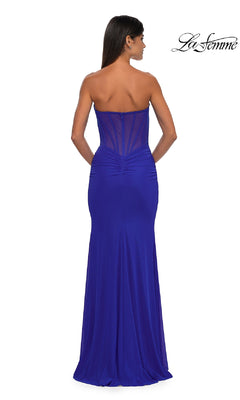 A woman models the La Femme 32734 Cut-Out Long Strapless Prom Dress in royal blue, featuring a sweetheart neckline, ruched details, a sheer back panel, and is posed facing away from the camera.