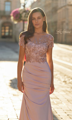 A woman stands outdoors in soft sunlight, wearing the La Femme 32737 long formal dress—light pink with an illusion neckline, lace embroidered bodice, short sleeves, and a flowing skirt.