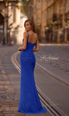 A woman wearing the Classic Long Beaded Prom Dress: La Femme 32753 stands on a cobblestone street, glancing over her shoulder.