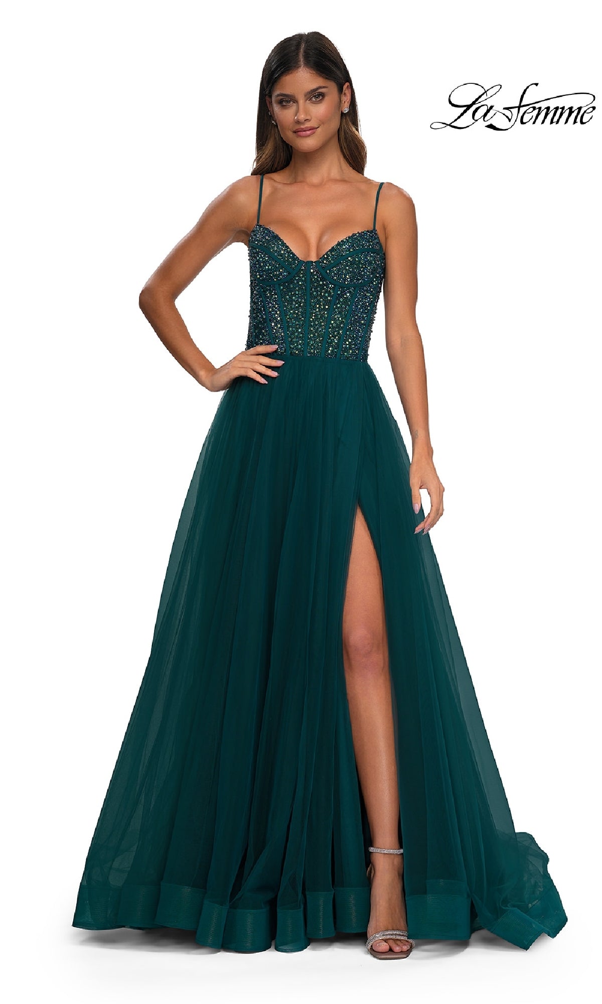 A woman wears the Beaded-Bodice Long Prom Dress: La Femme 32754, featuring a dark green hue, beaded bodice, spaghetti straps, and a thigh-high slit, as she stands against a white background.