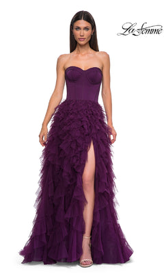A woman wears the Strapless Long Ruffled Prom Dress: La Femme 32760, featuring a corset-style bodice, thigh-high slit, and purple tulle A-line skirt, standing against a white background.
