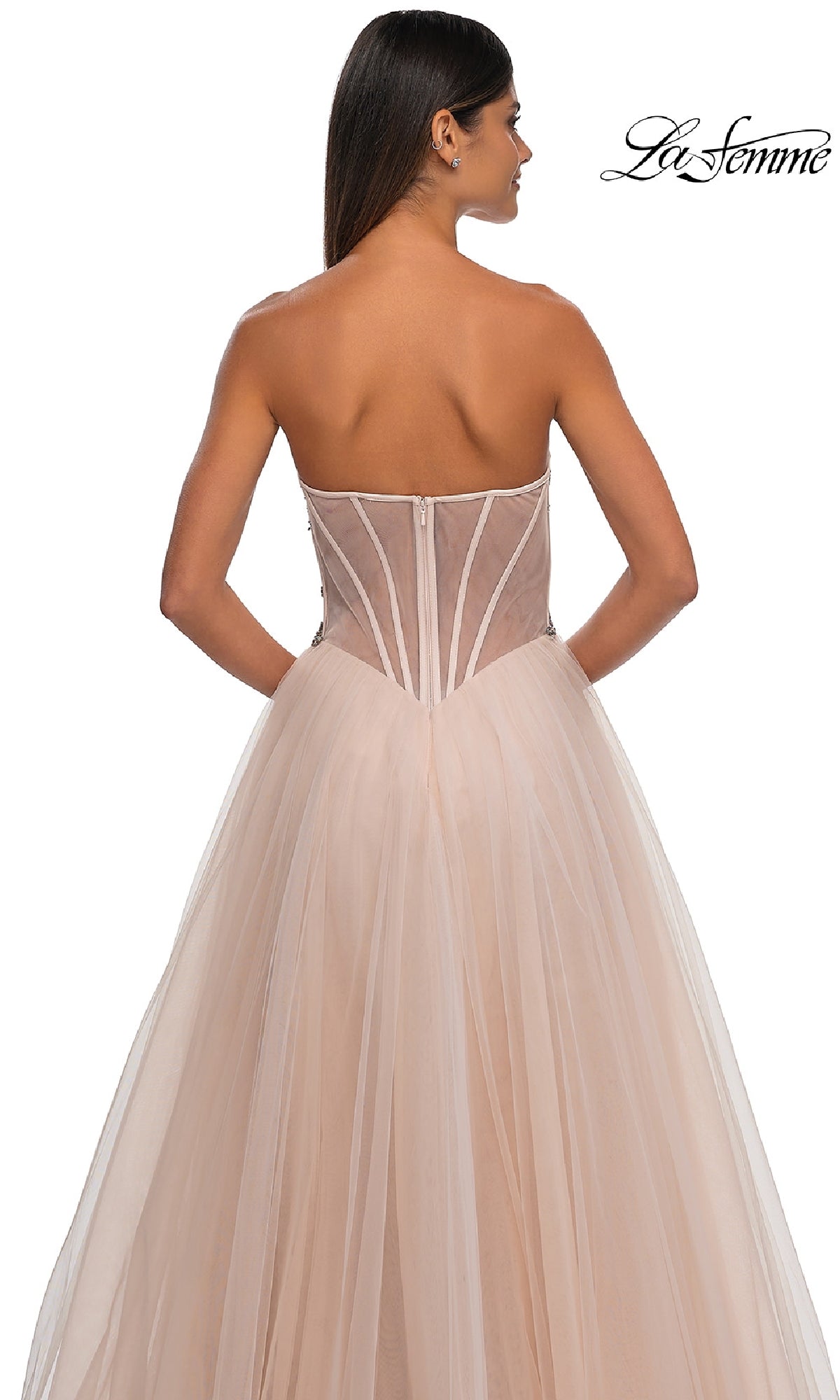 A woman wearing the Strapless Long Prom Ball Gown: La Femme 32767, featuring a sheer beaded corset bodice and flowing tulle skirt, is photographed from the back against a white background.