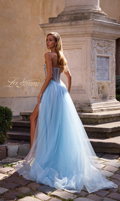 A woman in the La Femme 32767 strapless long prom ball gown with a sheer beaded corset back stands on a stone walkway before an ornate stone monument.