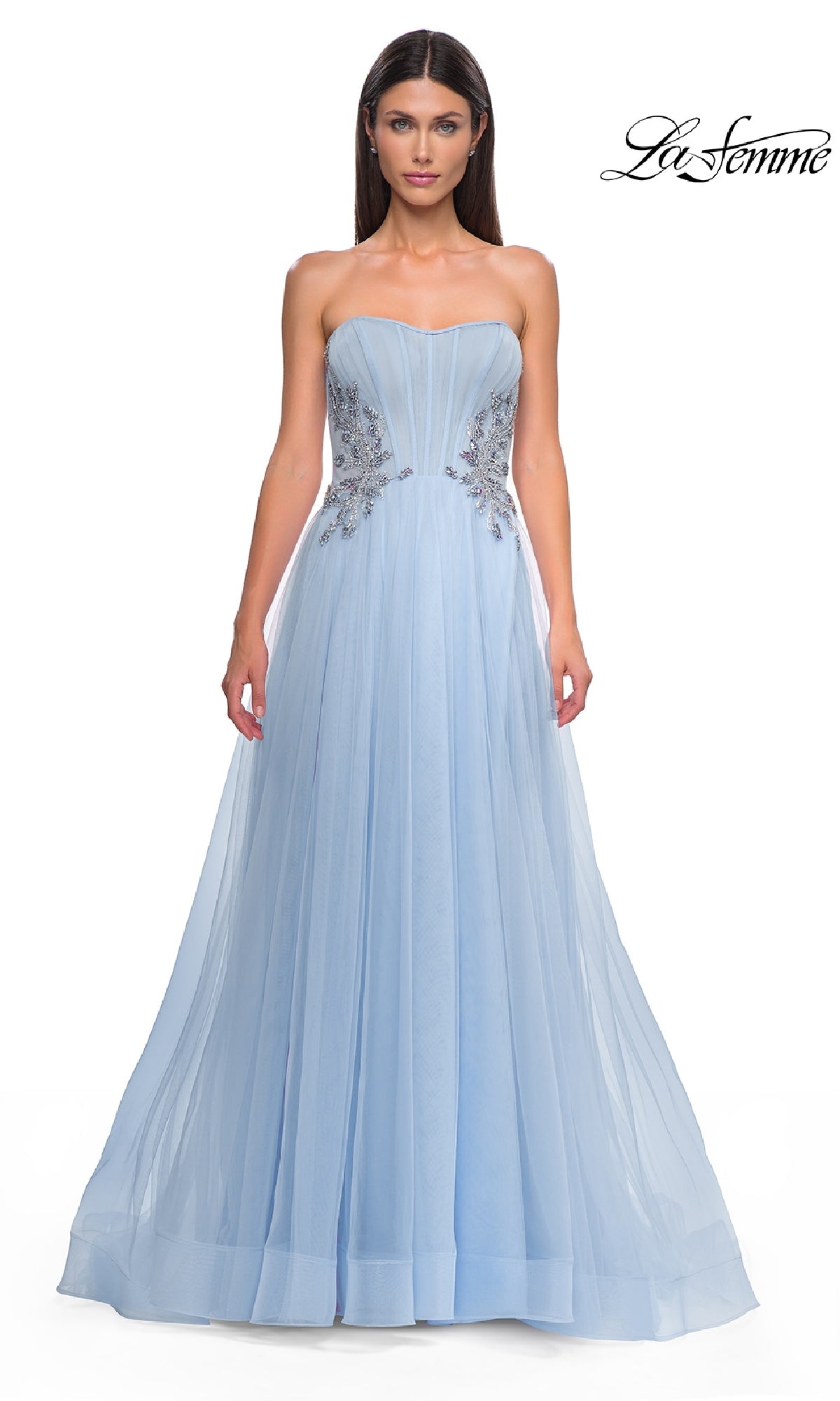 A woman wears the Strapless Long Prom Ball Gown: La Femme 32767, a floor-length light blue dress with silver floral bodice details, standing against a white background.