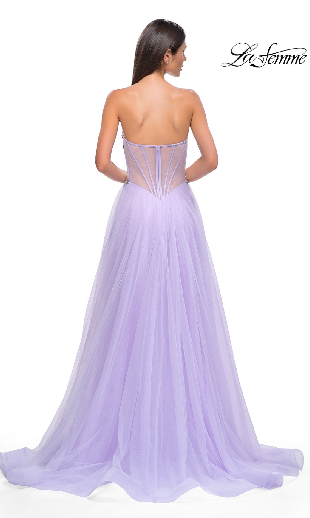 A woman stands with her back to the camera in the La Femme 32767, a strapless long prom ball gown featuring a floor-length lavender tulle skirt and sheer beaded corset bodice. The 