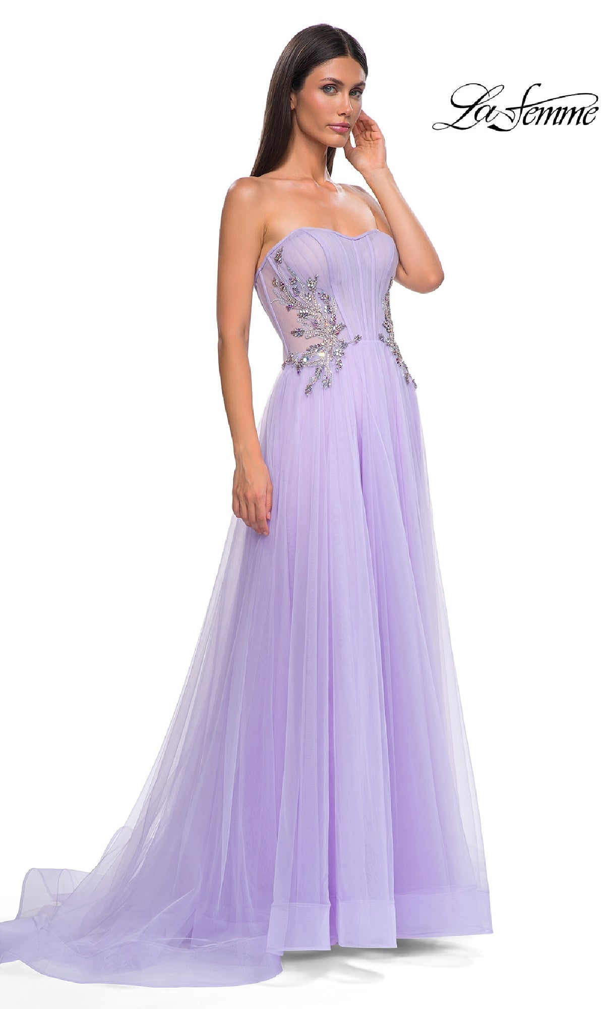 A woman stands against a white background wearing the Strapless Long Prom Ball Gown: La Femme 32767 in lilac, featuring floral embellishments and sheer bodice panels.