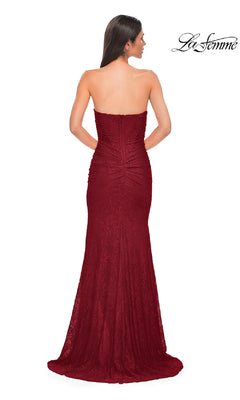 A woman faces away from the camera in a fitted, strapless La Femme 32773 long beaded prom dress. The floor-length gown in red features ruching at the back. The La Femme logo is visible in the top right corner.