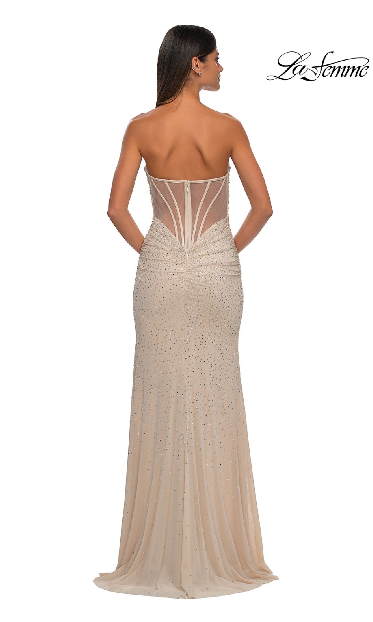 A woman faces away in the La Femme 32774, a strapless long beaded prom dress with sheer panels and rhinestone accents in a nude shade. The La Femme prom dress logo is in the top right corner.