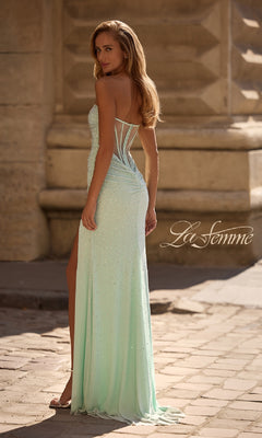 A woman in the La Femme 32774 strapless long beaded prom dress stands outdoors on a stone walkway, looking over her shoulder.