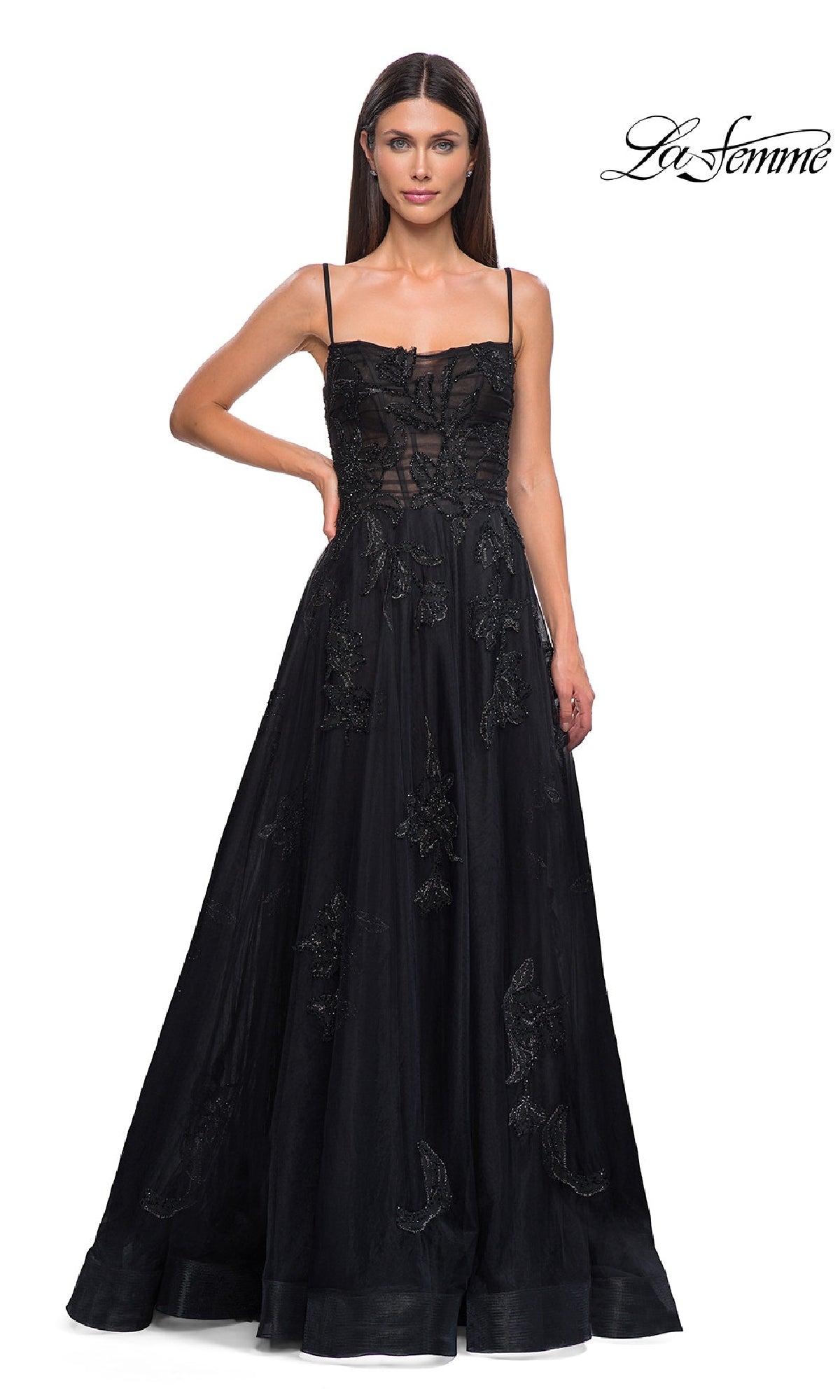 A woman models the La Femme 32781 long black glitter prom dress with thin straps and lace details, standing against a white background featuring the La Femme logo in the top right corner.