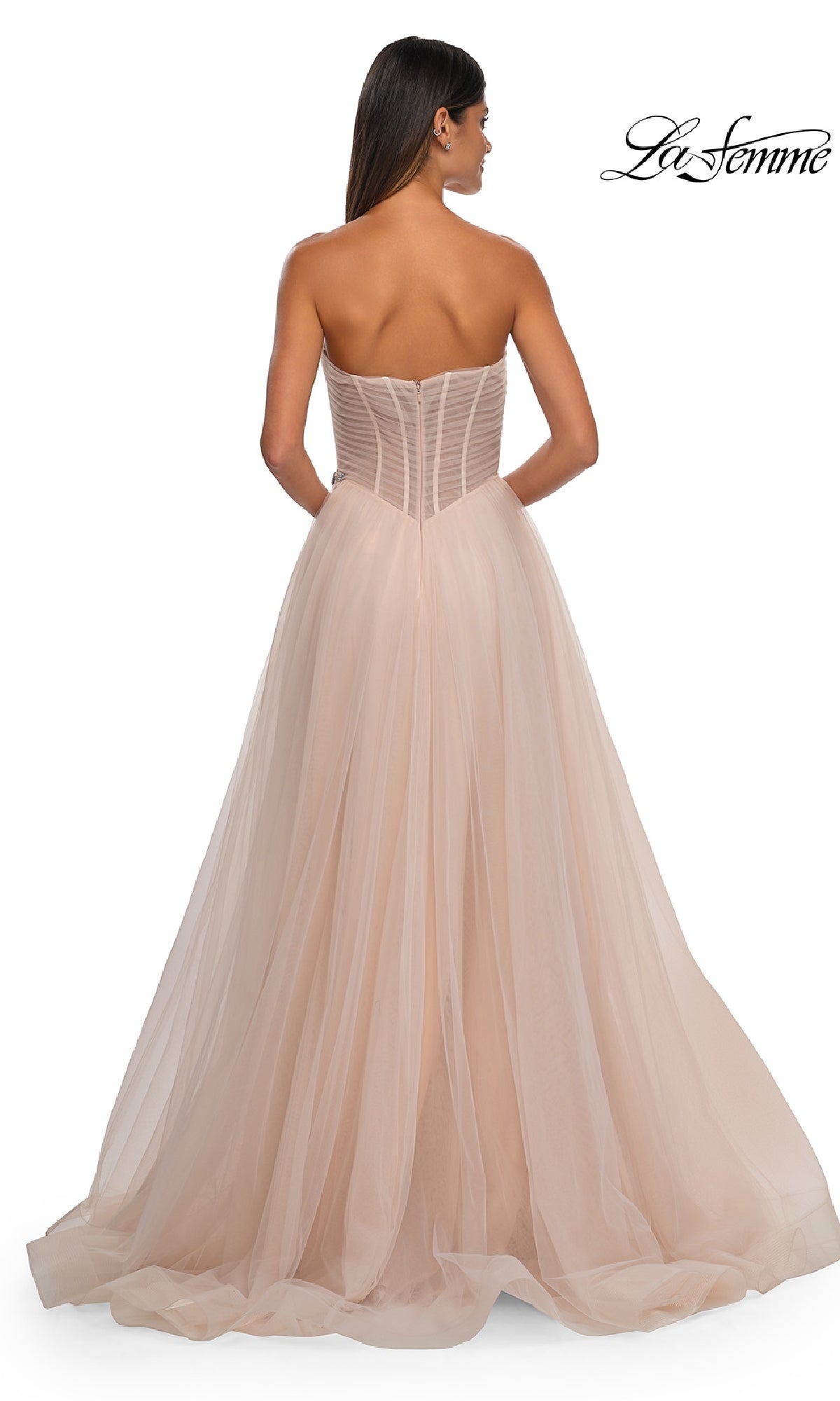 A woman in the La Femme 32789 strapless long prom ball gown stands with her back to the camera. The light pink tulle dress flows to the floor and features a fitted sweetheart bodice for timeless elegance.