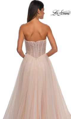A woman models the Strapless Long Prom Ball Gown: La Femme 32789 in blush pink, featuring a fitted semi-sheer sweetheart bodice, flowing tulle skirt, rhinestone floral accents, and the La Femme logo at the top right. Shown from the back.