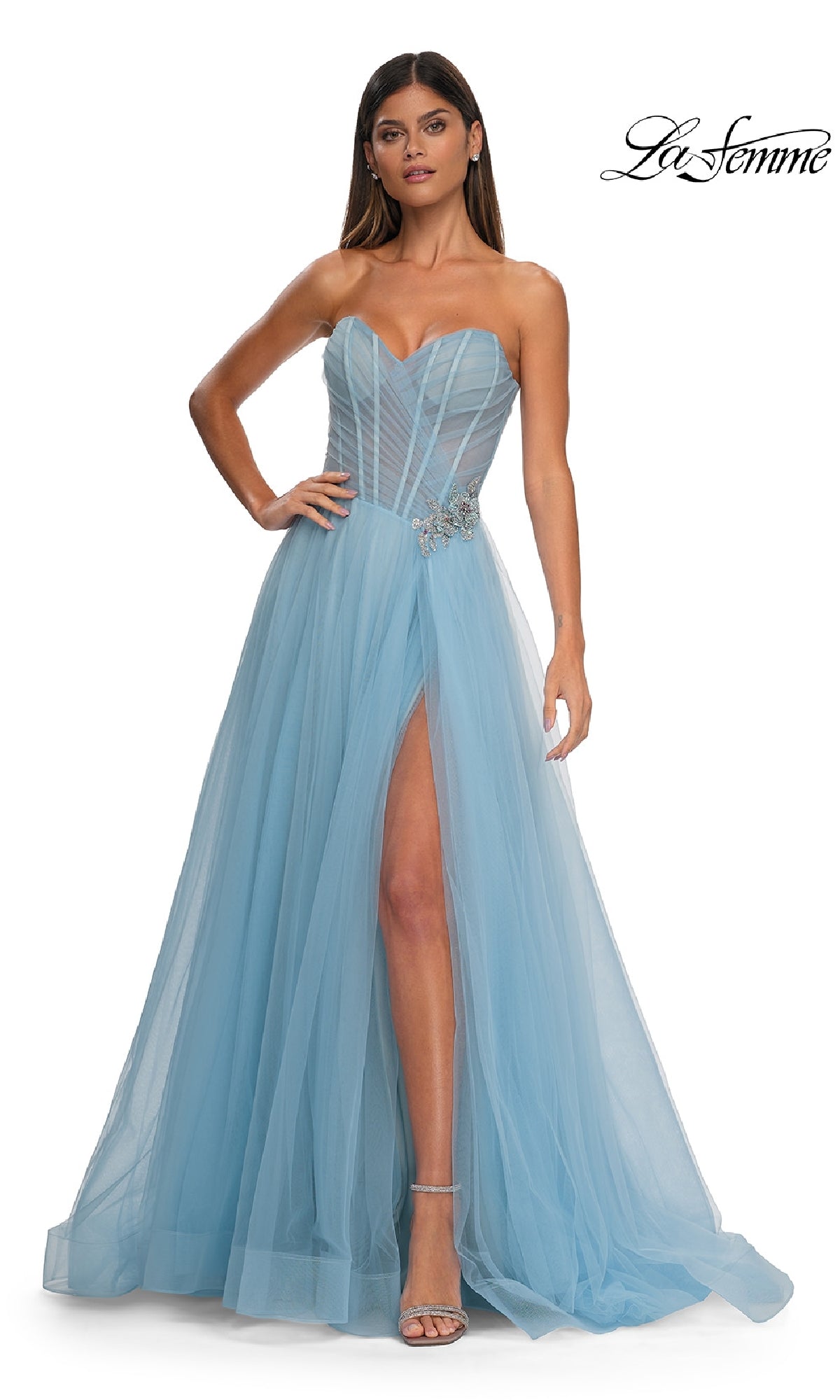 A woman wears the La Femme 32789 strapless long prom ball gown in light blue, featuring a sheer sweetheart bodice, high slit, tulle skirt, and rhinestone floral waist. She finishes the look with strappy heels.