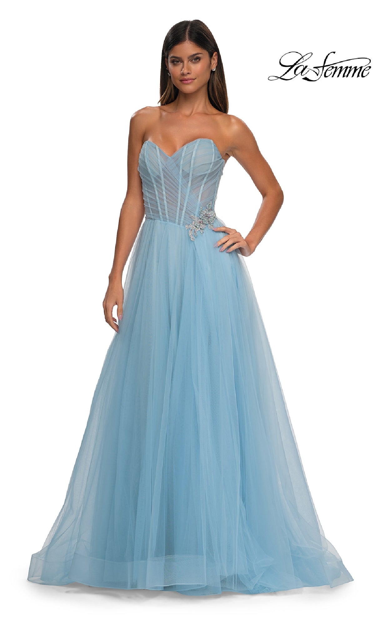 A woman wears the Strapless Long Prom Ball Gown: La Femme 32789, a light blue tulle dress with a sweetheart bodice and rhinestone floral detail at the waist.