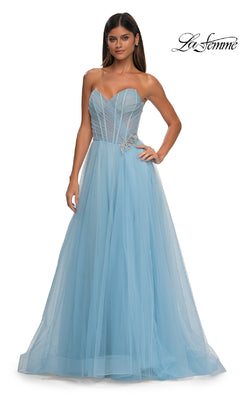 A woman wears the Strapless Long Prom Ball Gown: La Femme 32789, a light blue tulle dress with a sweetheart bodice and rhinestone floral detail at the waist.