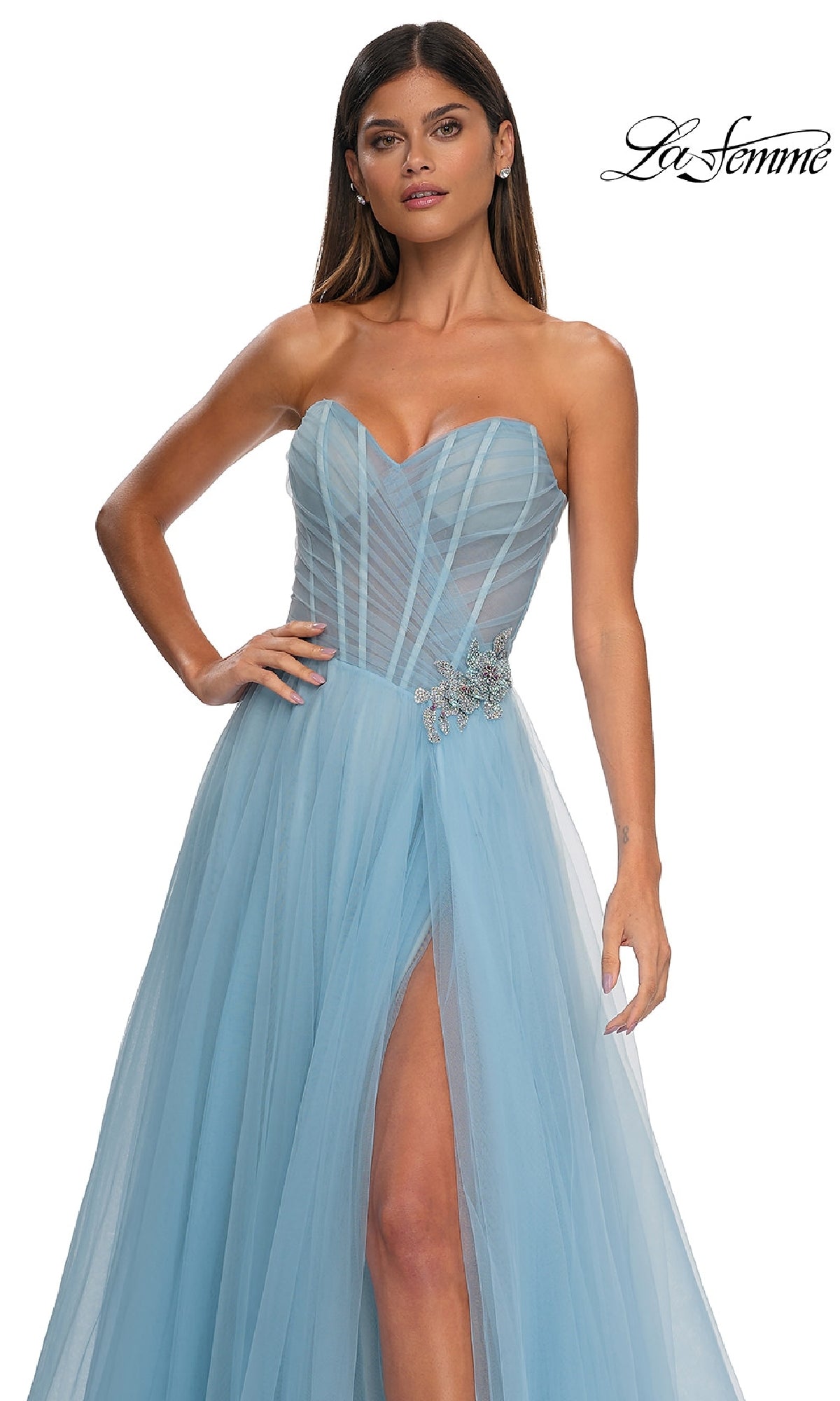 A woman wearing the La Femme 32789 Strapless Long Prom Ball Gown in light blue tulle, featuring a sweetheart bodice, high slit, sheer details, and sparkling rhinestone floral waist accents.